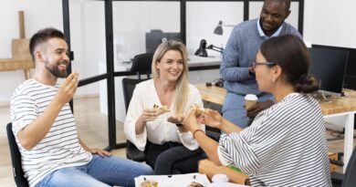 Quatro colaboradores sorridentes em ambiente de escritório moderno compartilhando uma pizza durante o intervalo, representando a satisfação com o benefício alimentação refeição empresa